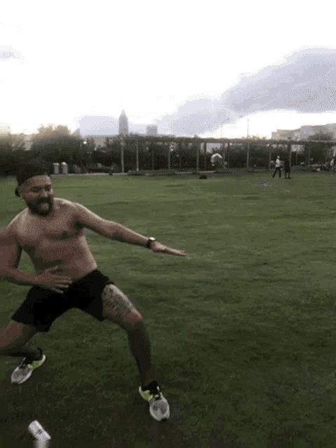 a shirtless man with a tattoo on his leg is jumping in the grass