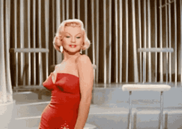 a woman in a red dress is standing in front of a fence