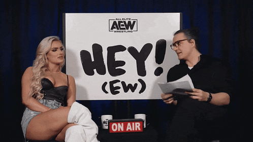a man and a woman sit in front of a sign that says hey ( ew )