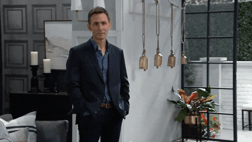a man in a suit and blue shirt is standing in a living room with his hands in his pockets