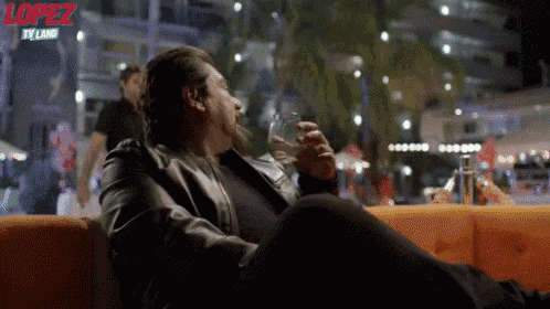 a man is sitting on a couch drinking a glass of water with the words lopez tv land on the bottom