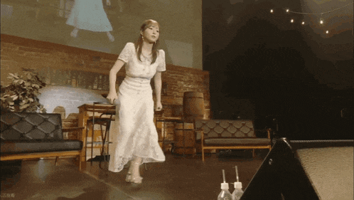 a woman in a white dress stands on a stage in front of a large screen