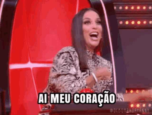 a woman is sitting in a red chair and laughing while saying ai meu coração .