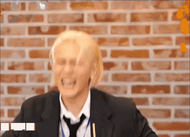 a man in a suit and tie is laughing in front of a brick wall