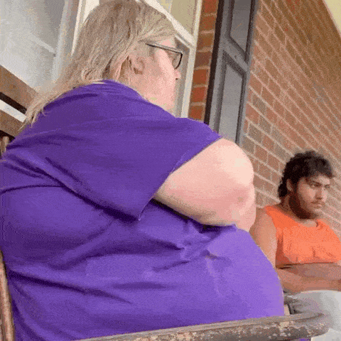 a woman in a purple shirt is sitting on a porch next to a man in an orange tank top .