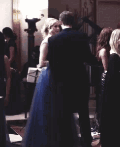 a man in a suit and a woman in a blue dress are standing in a room
