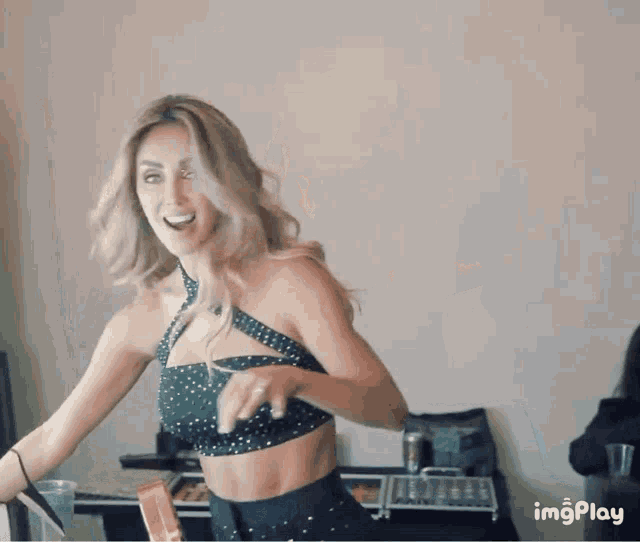 a woman in a crop top is dancing in front of a wall that says imgplay on the bottom