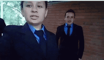 two men in suits and ties are standing next to each other in front of a brick wall