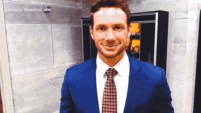a man in a suit and tie is smiling in front of a general hospital sign