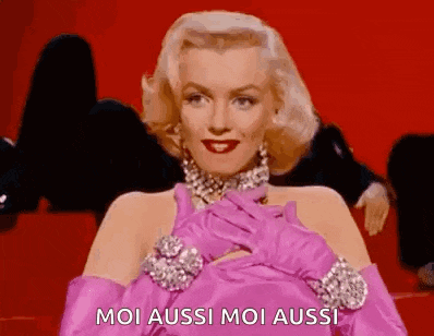 marilyn monroe is wearing pink gloves and a pink dress and is sitting on a red carpet .