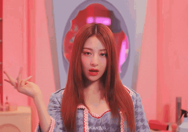 a woman with red hair is standing in front of a pink wall with the word nanen on the bottom