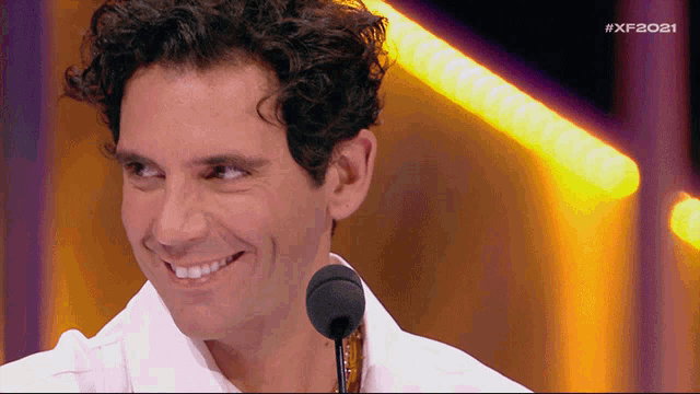 a man with curly hair is smiling in front of a microphone with the hashtag #xf2021 on the bottom right
