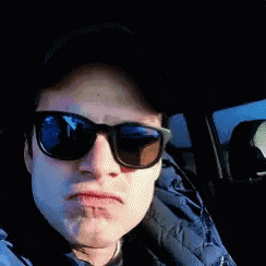 a man wearing sunglasses and a hat is sitting in a car making a funny face .