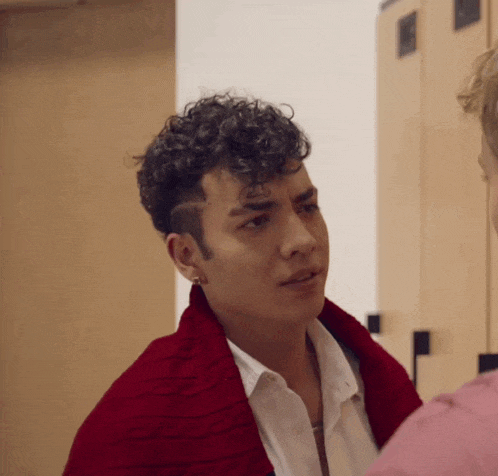 a young man with curly hair is wearing a red sweater