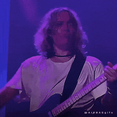 a man in a white shirt is playing a guitar in a purple light