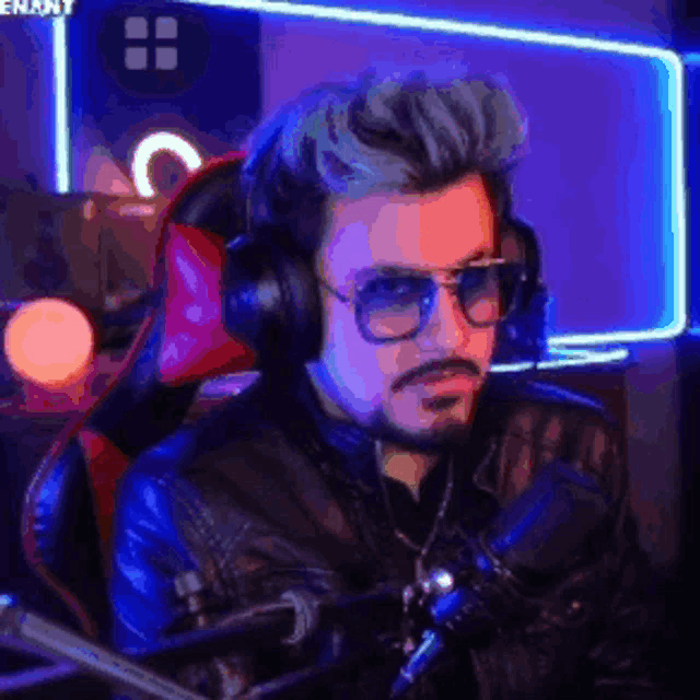 a man wearing headphones and sunglasses is sitting in front of a microphone in a dark room .