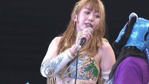 a woman singing into a microphone next to another woman wearing a blue mask