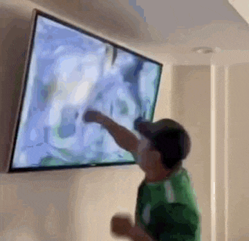 a man in a green shirt is pointing at a television .