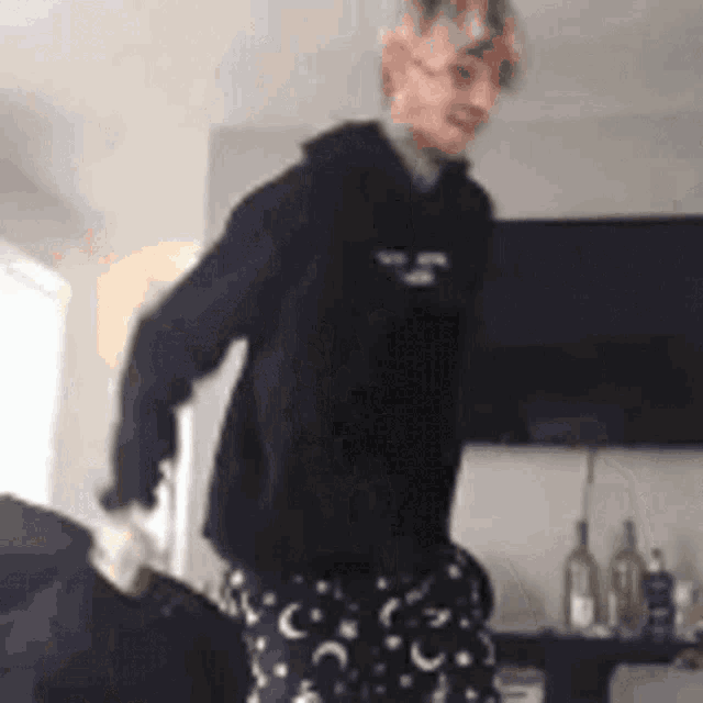 a person wearing a black hoodie and pajama pants is standing in a living room .