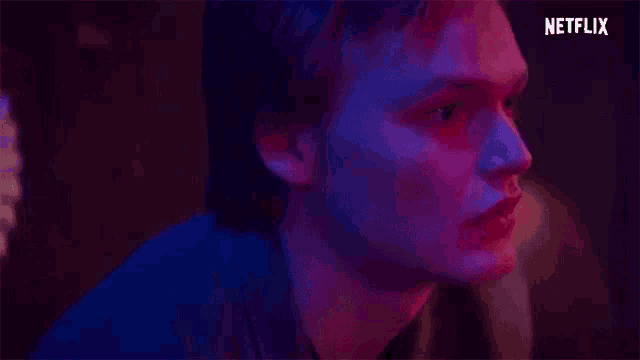 a close up of a man 's face in a dark room with red and blue lights behind him .