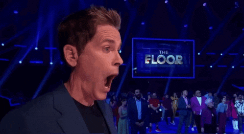 a man is standing on a stage with his mouth open in front of a large screen that says the floor .