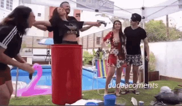a group of people are standing around a pool with a red barrel in the middle