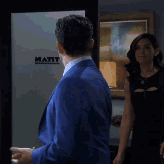 a man in a blue suit is standing in front of a wall that says matit