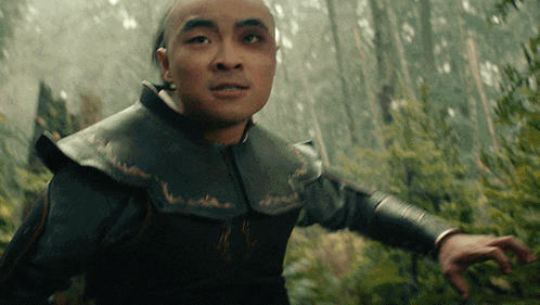 a man with a black eye is standing in the woods with his arm outstretched