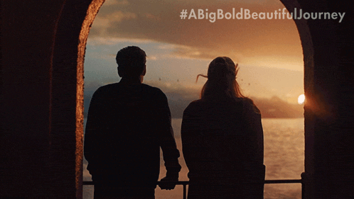 a man and a woman are holding hands while looking out at the ocean