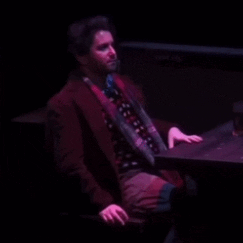 a man in a red coat and tie is sitting at a table in the dark .