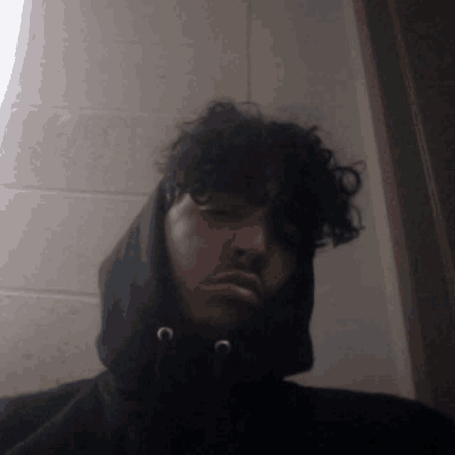 a man with curly hair wearing a black hooded sweatshirt