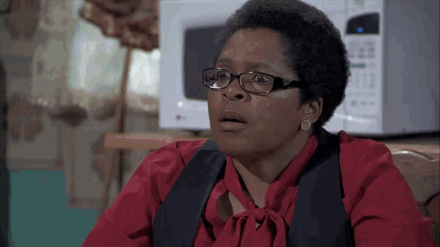 a woman wearing glasses and a red shirt is sitting in front of a microwave
