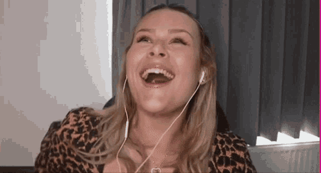 a woman wearing headphones is laughing with her mouth open while sitting on a couch .