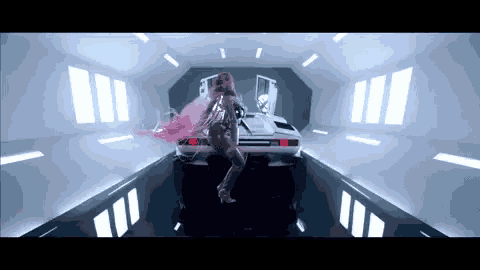 a woman with long pink hair is dancing in front of a car in a room .
