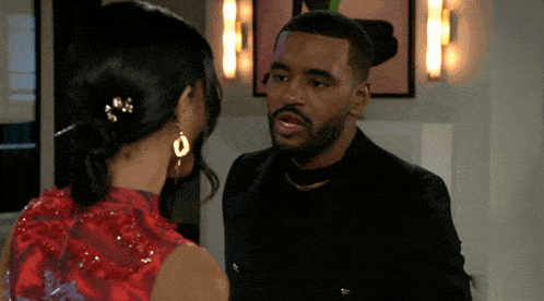 a man in a black suit and a woman in a red dress look at each other