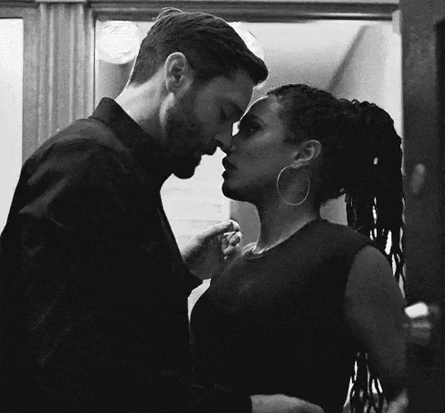 a black and white photo of a man and woman kissing in a room .