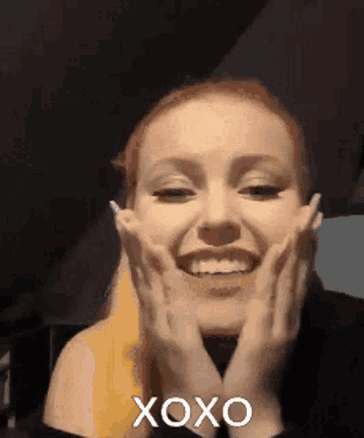 a woman is smiling and holding her face with her hands and says xoxo