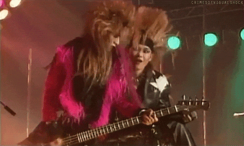 a man in a pink fur coat is playing a bass guitar on stage .