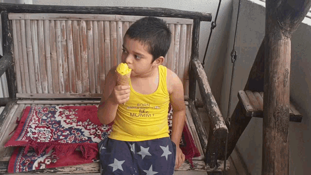 a young boy eating an ice cream cone wearing a yellow tank top that says born to be mommy