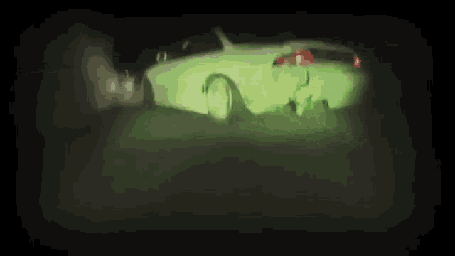 a white car is driving down a dark street at night and is glowing green .