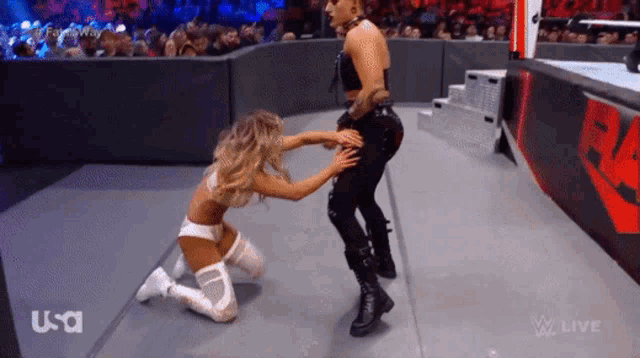 two women are kneeling down in a wrestling ring and one of them is touching the butt of the other .