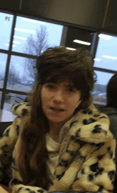 a woman wearing a leopard print coat is sitting in front of a window