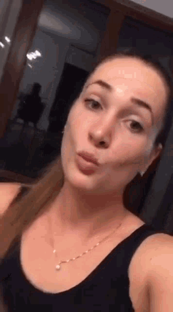 a woman in a black tank top and necklace is taking a selfie in front of a mirror .