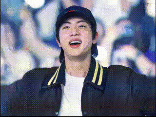 a man wearing a baseball cap and a jacket is standing in front of a crowd .