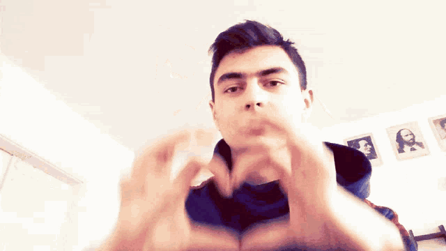 a man making a heart shape with his hands in front of a wall with pictures on it