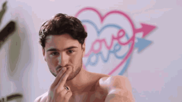 a shirtless man is taking a selfie in front of a heart with the word love on it