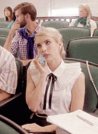 a woman is sitting in a lecture hall talking on a cell phone