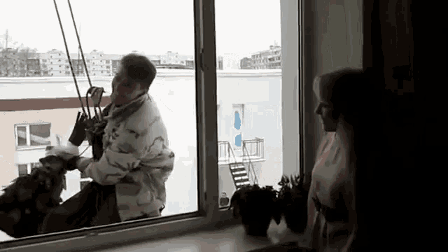 a man is hanging from a rope while a woman looks out a window