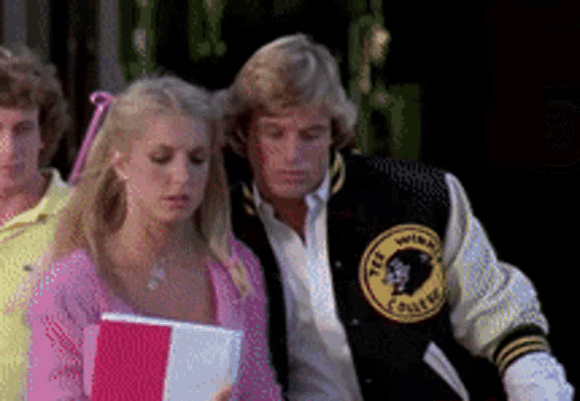 a man wearing a varsity jacket with the word college on it stands next to a woman