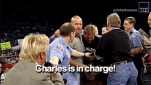 a man in a black shirt is being held by a police officer and says charles is in charge